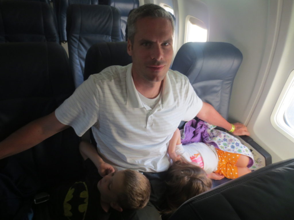 2 kids sleeping on dads lap after a red eye flight