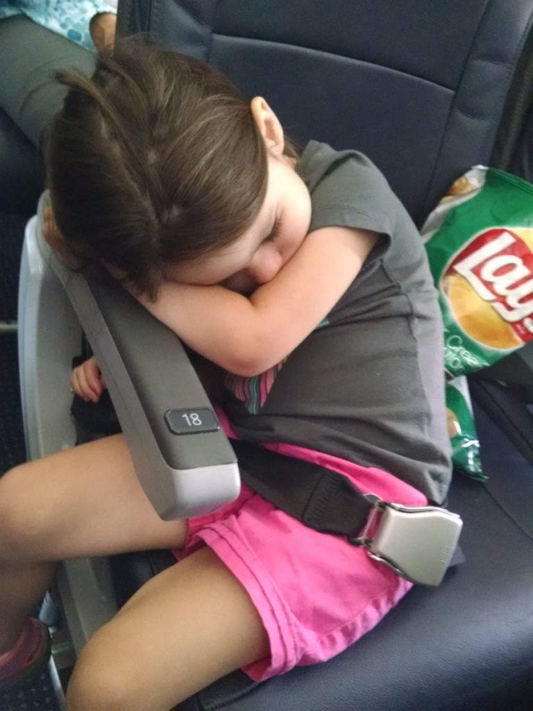 A girl sleeps on an airplane leaning on the armrest