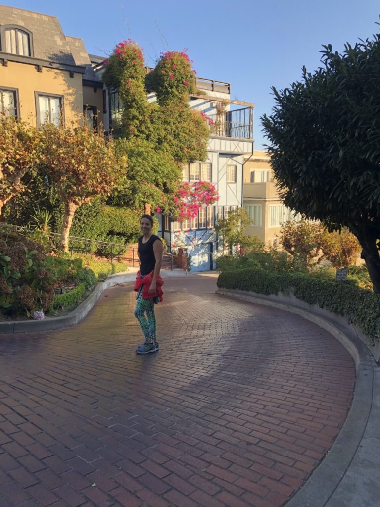A woman walks down Lombard Street with beautiful flowers on a home in the background in San francisco
