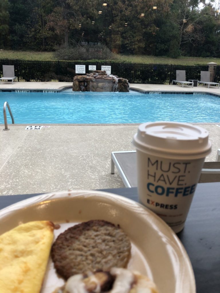 A plate of Breakfast and coffee with the view of a pool at Holiday Inn and Suites in Conroe, Texas