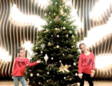 2 girls stand in front of the Christmas tree having family fun at the Westin DFW airport