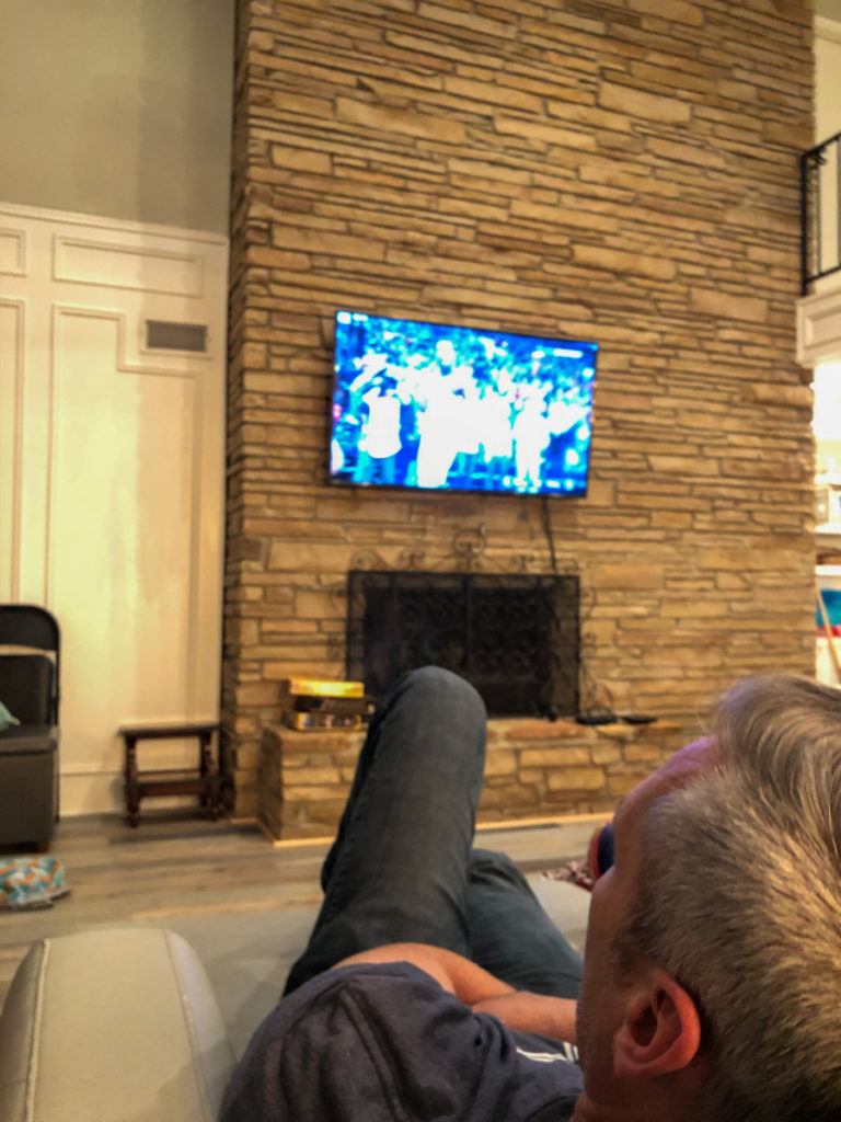 Man watches basketbal while stretched out on a couch at Texoma Luxury Rentals