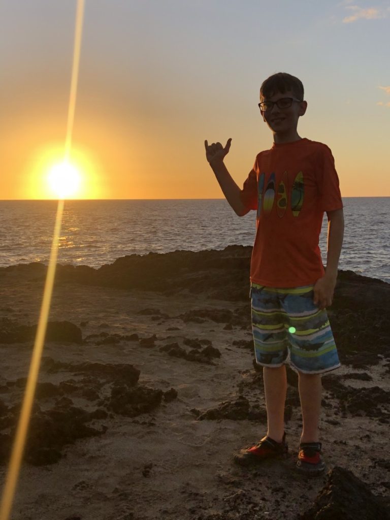 A young Boy with 'hang loose' sign at Hawaiian Sunset.