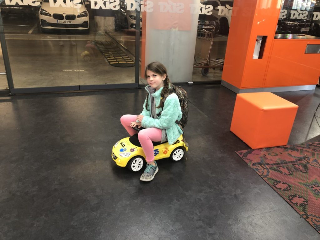 Young Girl sitting on a small car at a Rental Car Office in Barcelona