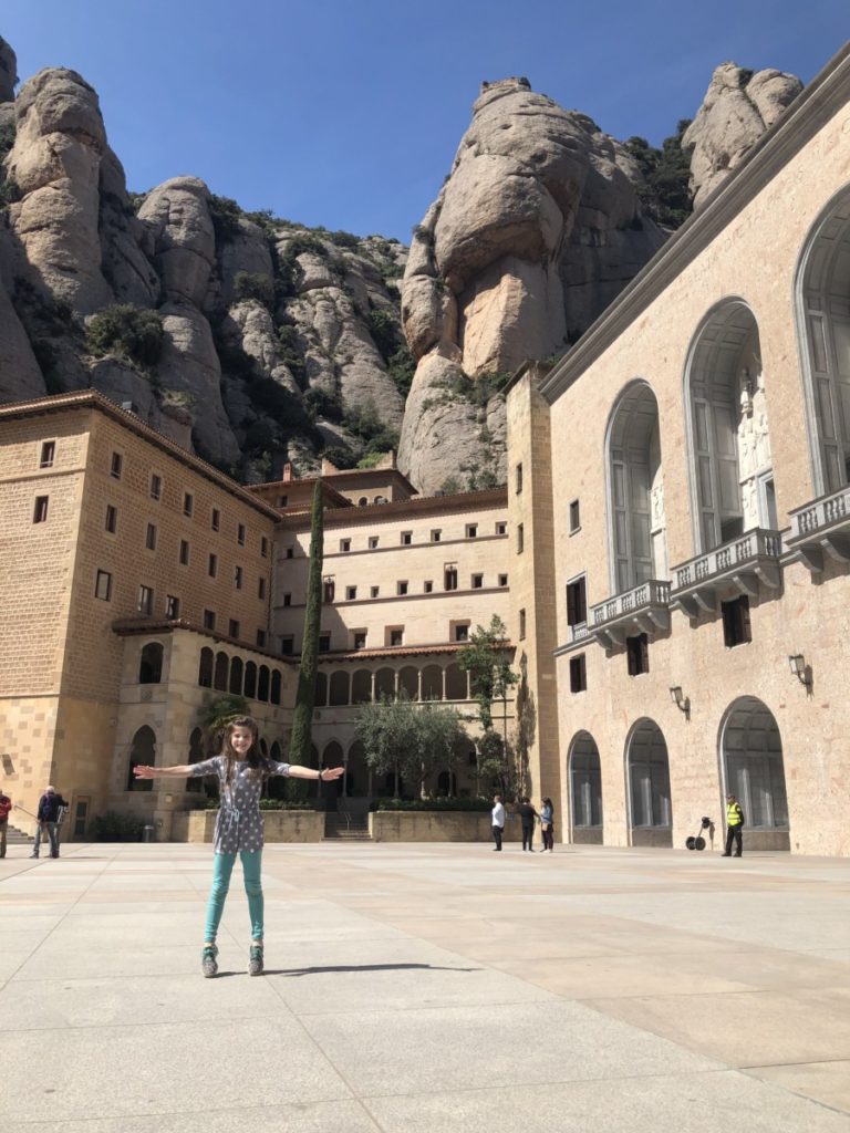 Young girl jumping in front of the monastery built in the mountains, Montserrat, Spain