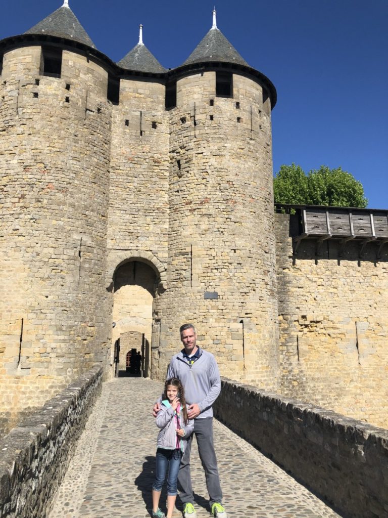 Dad and daughter in from of a 3 turret castle wall at Carcassone France