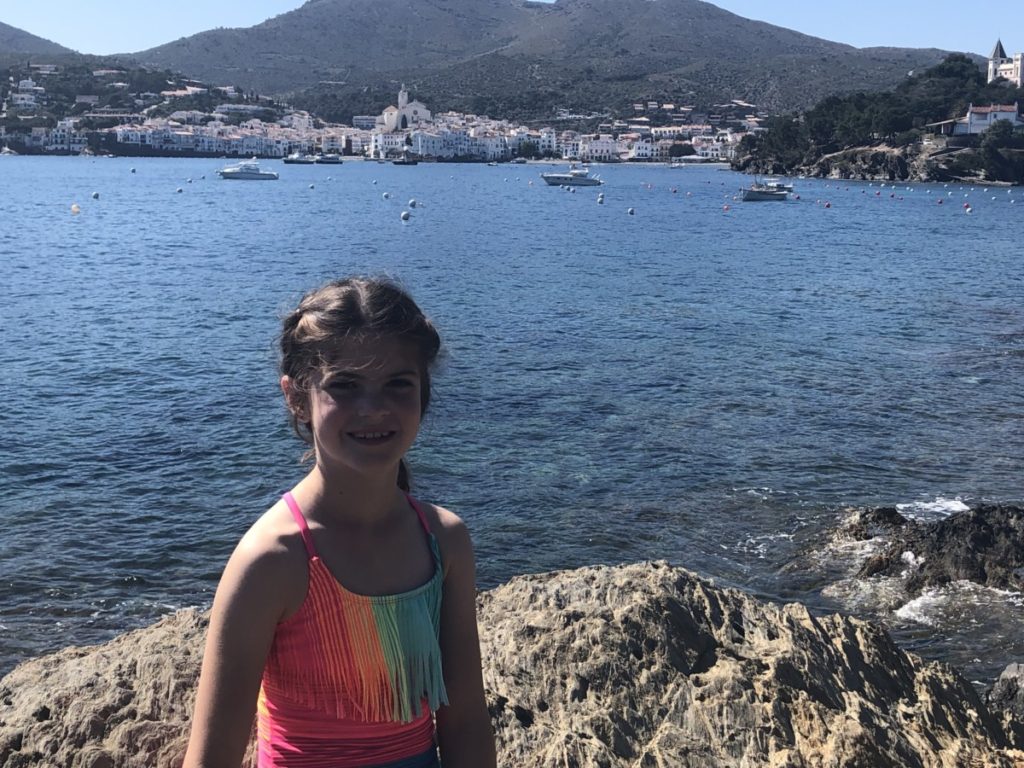 Young girl in swimsuit overlooking bay and the city of Cadaques in Costa Brava, Spain near Barcelona