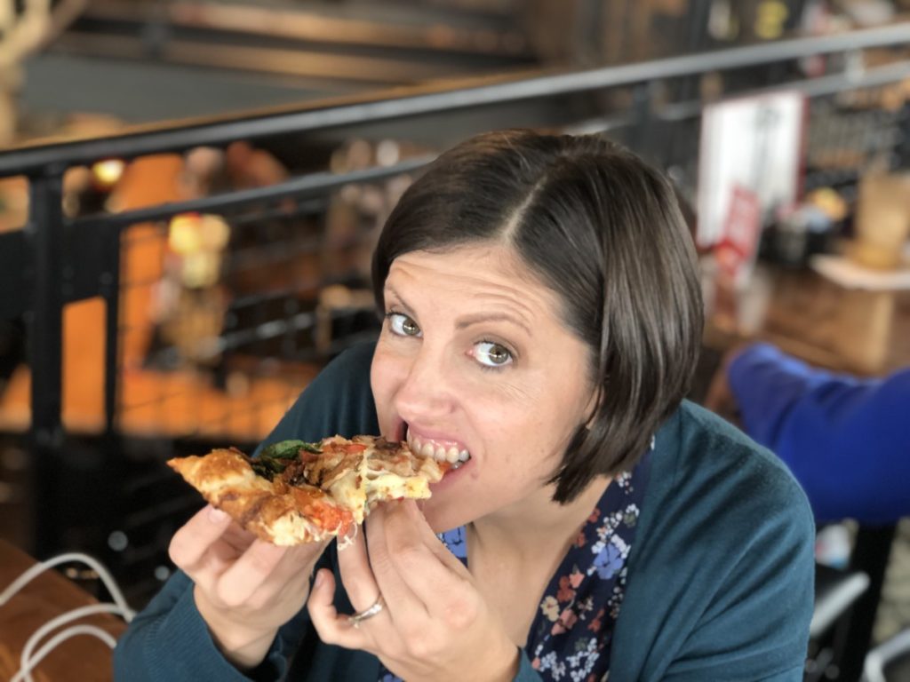 A woman eats a slice of cheesy pizza at Hideaway pizza in OKC