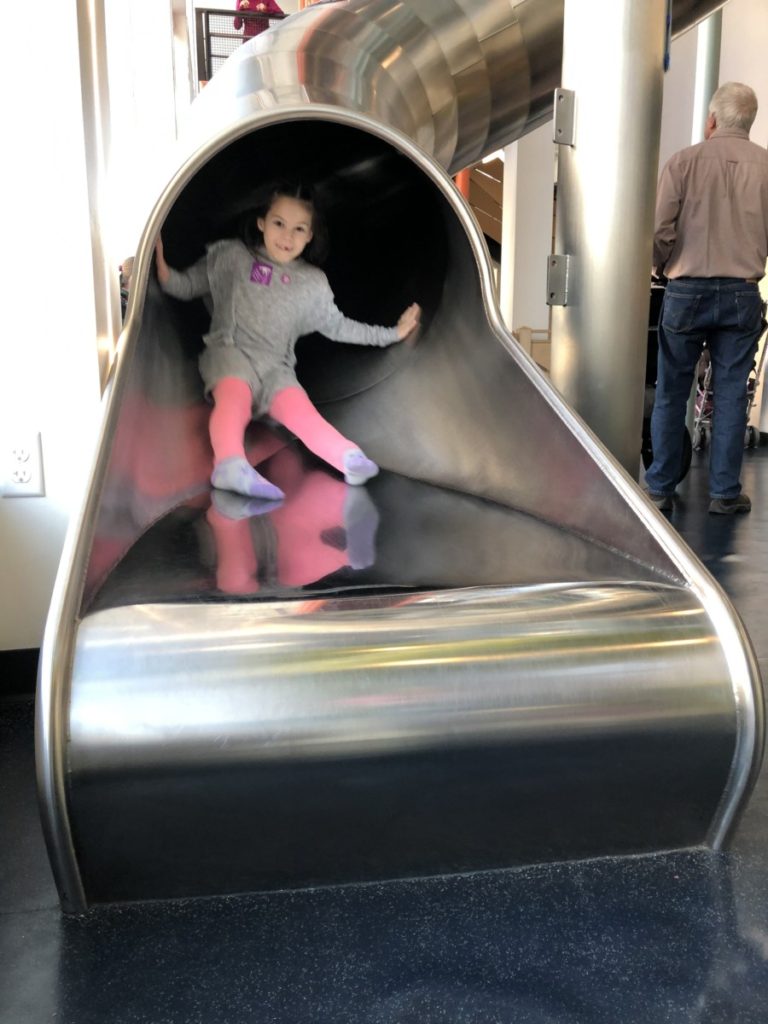 Girl slides out the bottom of a 3 story curly slide at the Minnesota Children's Museum