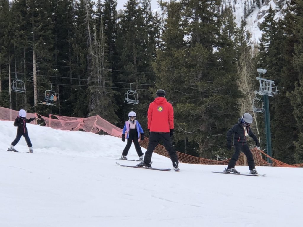 Brighton Ski Resort Ski school instructor teaches 3 kids to ski down the bunny hill