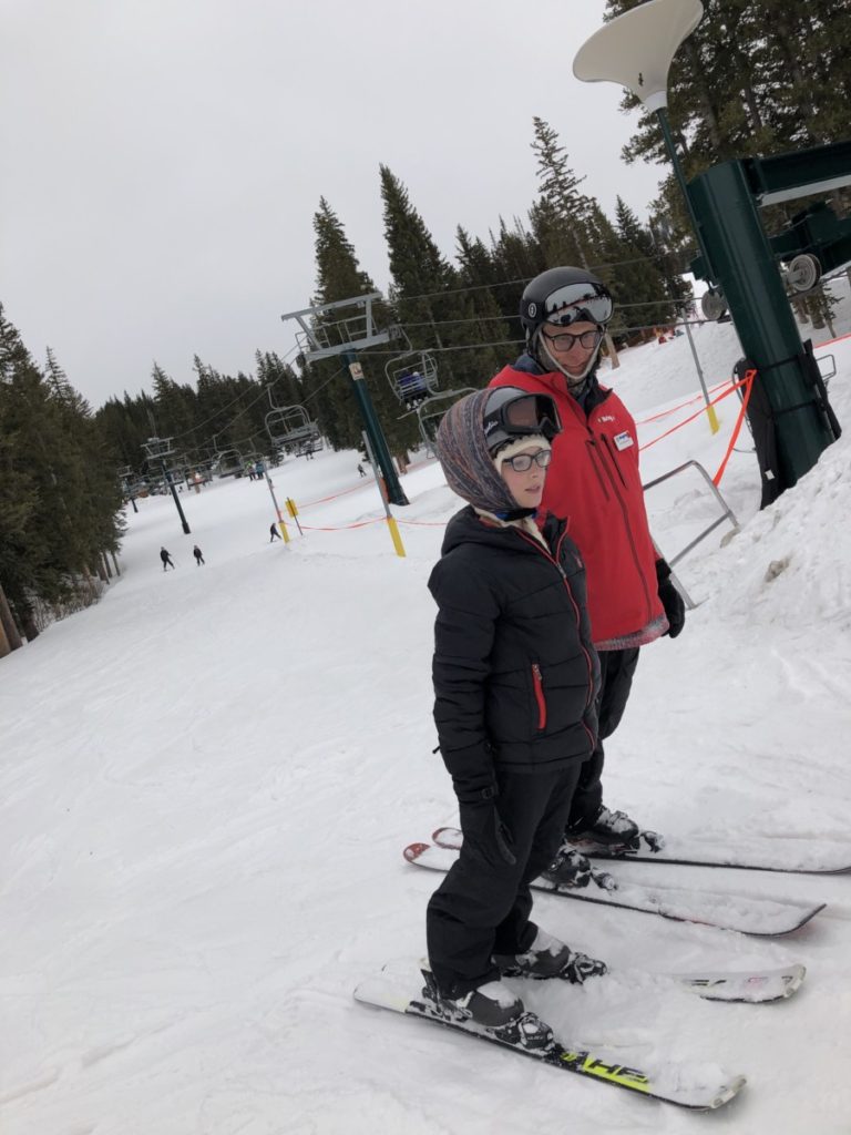 Boy leaning forward on his skis with his ski teacher with ski lift in the background at Brighton Ski Resort