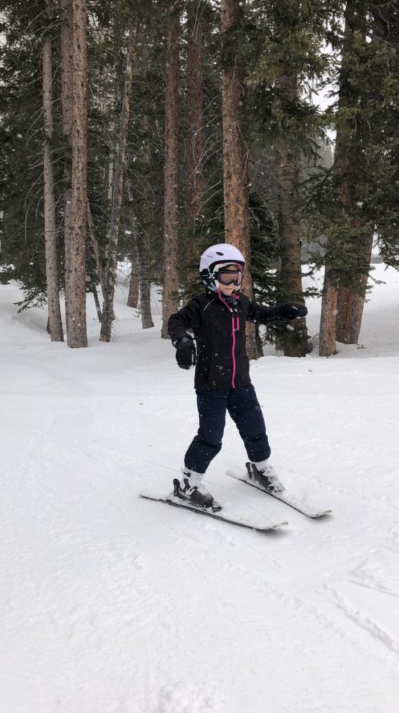 young girl skis in front of trees at Brighton ski Resort