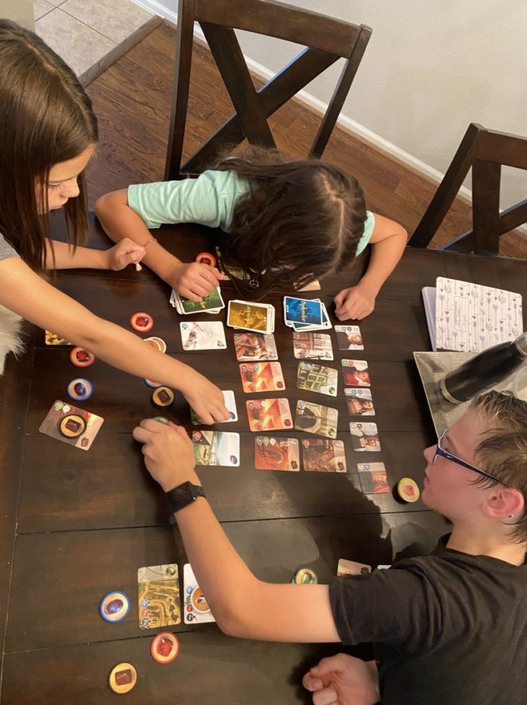 3 kids reach for gems and cards during a game of splendor