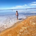 A young girls stands at the edge of the Great Salt Lake and the yellow and gold swirling sand on the beach