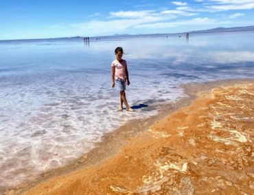 A young girls stands at the edge of the Great Salt Lake and the yellow and gold swirling sand on the beach