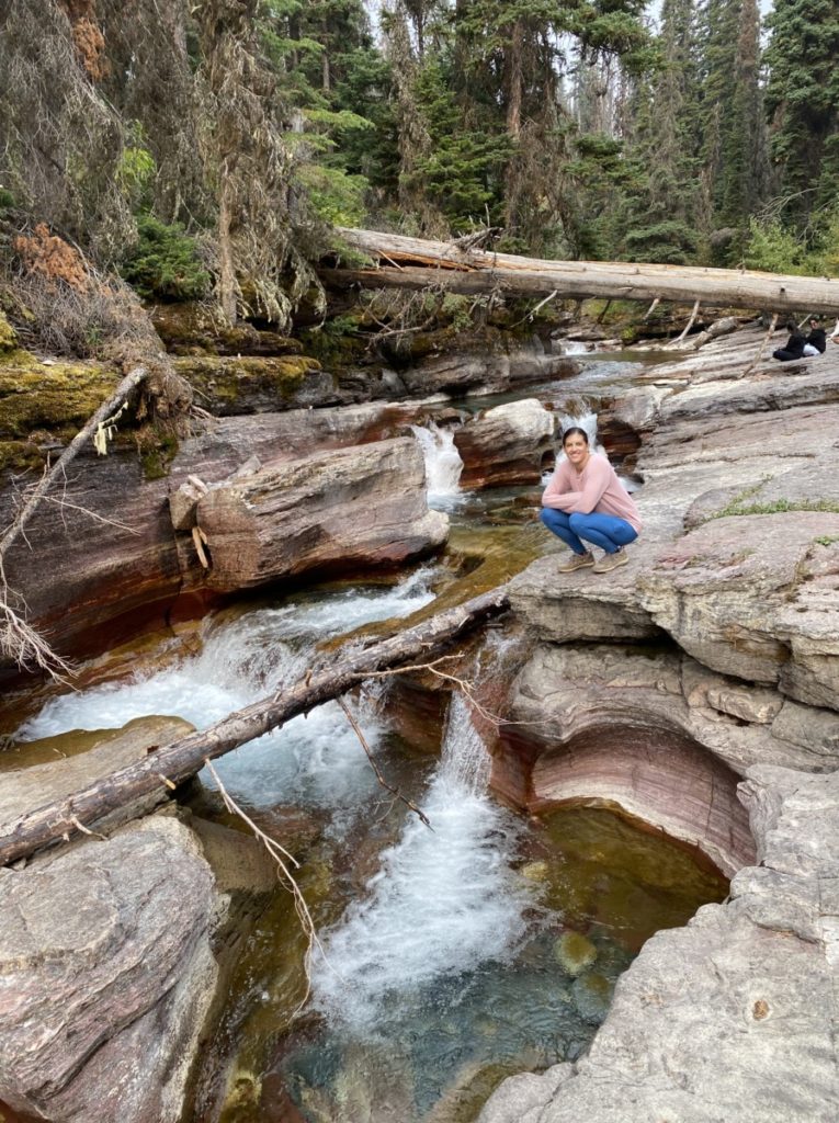 woman sits above a waterfall in a gorge of clear water along the Florence Falls HIking Trail in Glacier National Park