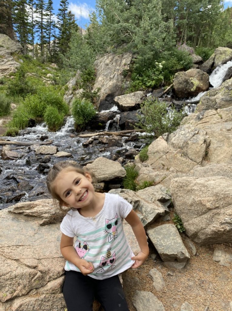 A toddler grins in front of a river in Rocky Mountain National Park