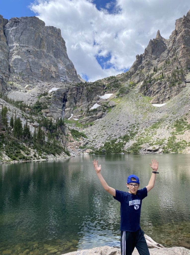 A boy stand triumphant at the end of a hike to Emerald Lake at the base of Rocky Mountains