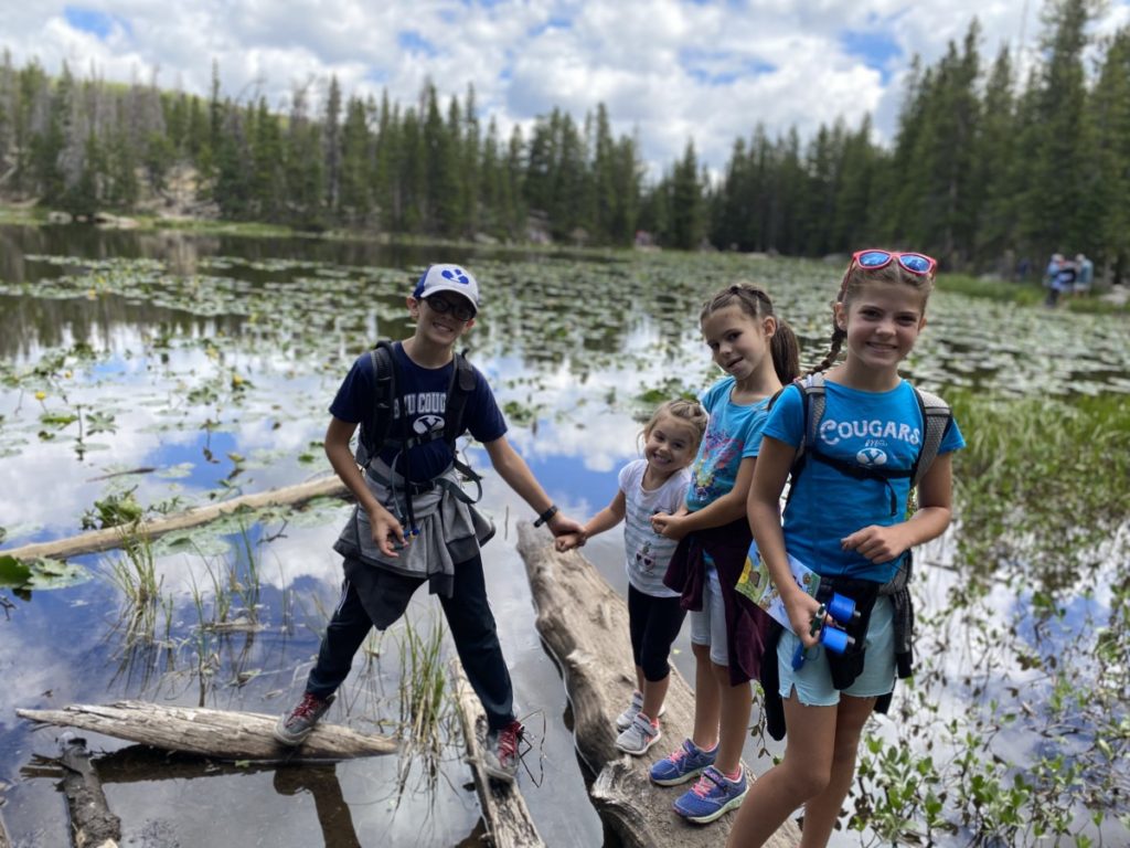 4 kids standing on a sunken log at Nymph Lake in Rocky Mountain National Park