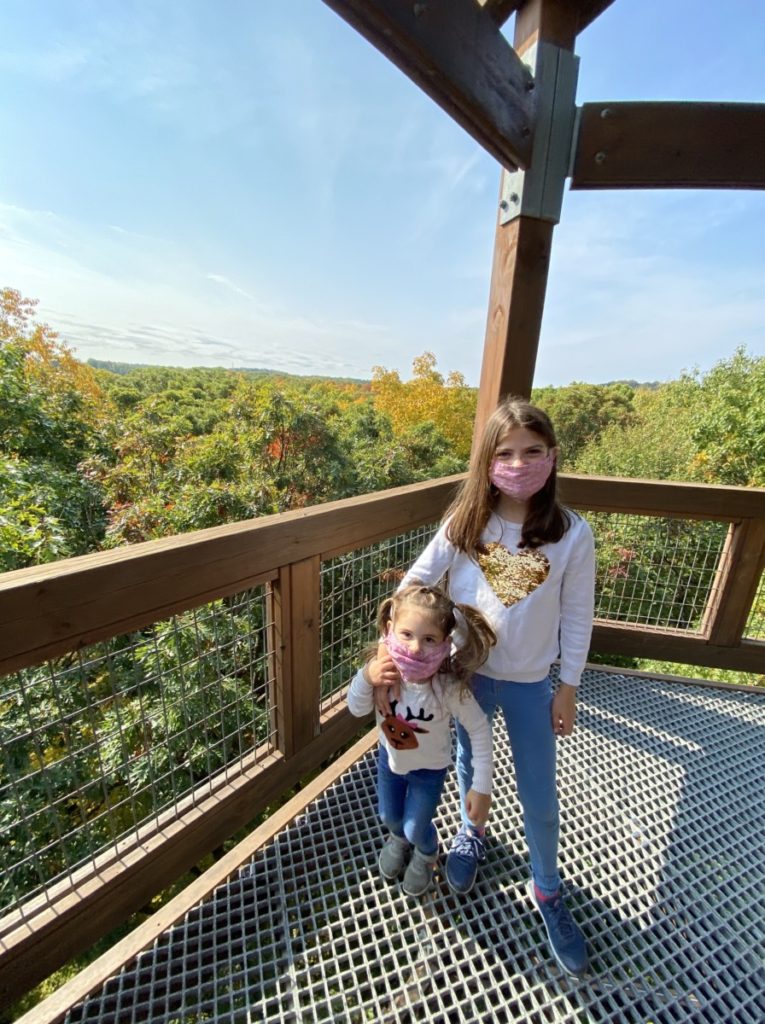2 girls in masks on the Tower platform at Holden Arboretum and tree tops in the background