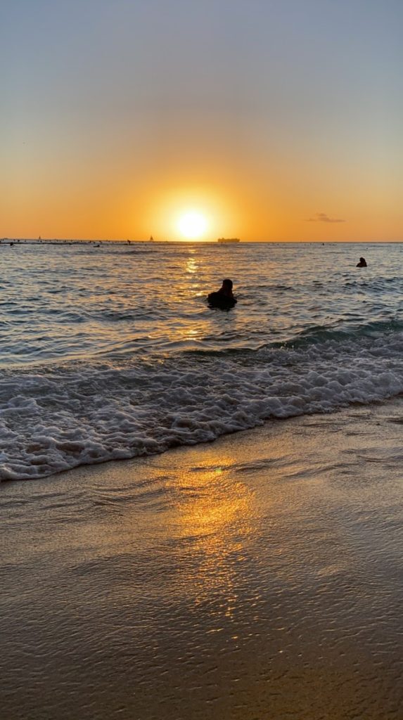 The sun on the horizon creating an orange glow sunset on Waikiki while a boogie boarder floats in the water