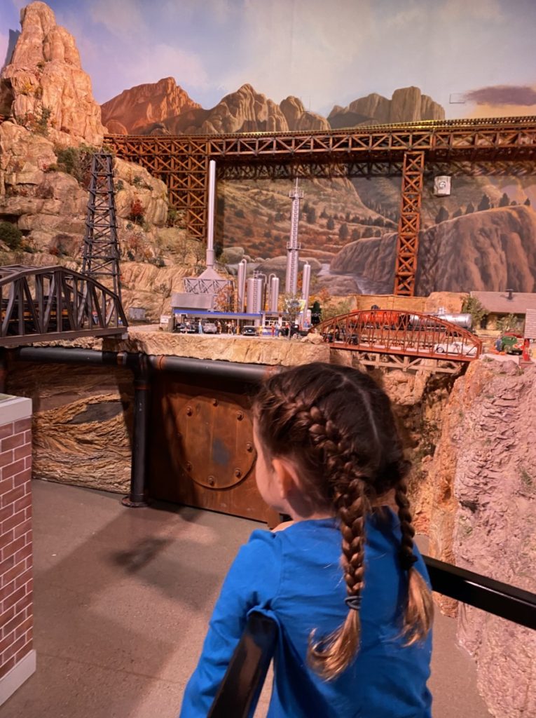 A girl in 2 braids looks over the miniature train display at Traintopia in Frisco, Texas