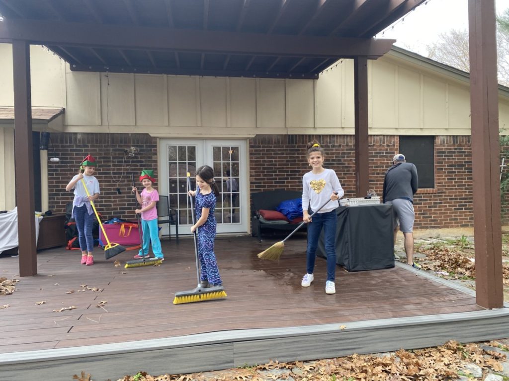 4 young girls sweep a porch while dad rakes leaves for christmas service