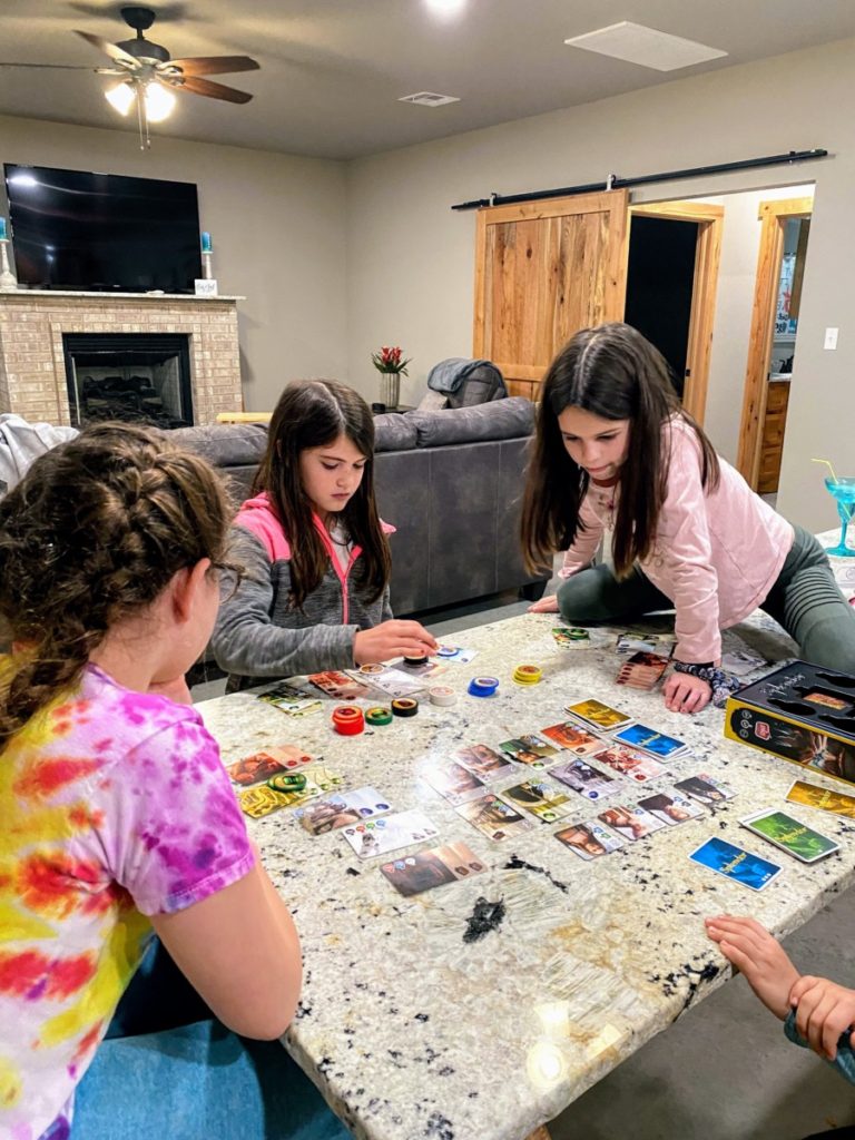 3 girls play a board game, splendor at a cabin