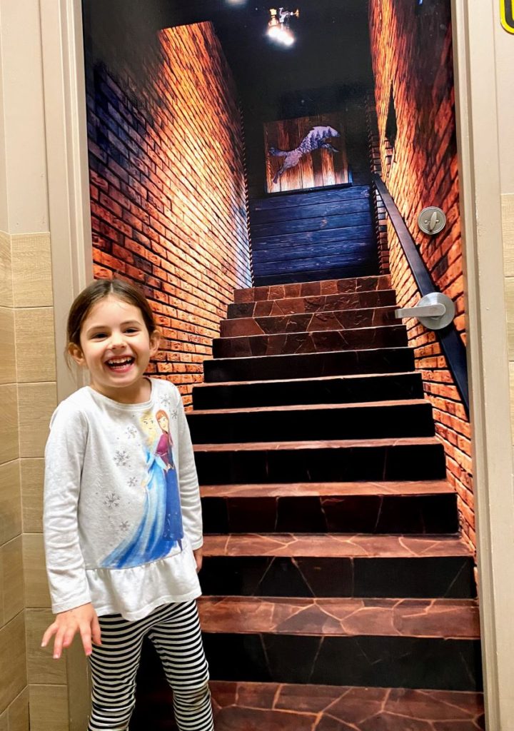 Young Girl shows Brew St Bakery bathroom door illusion