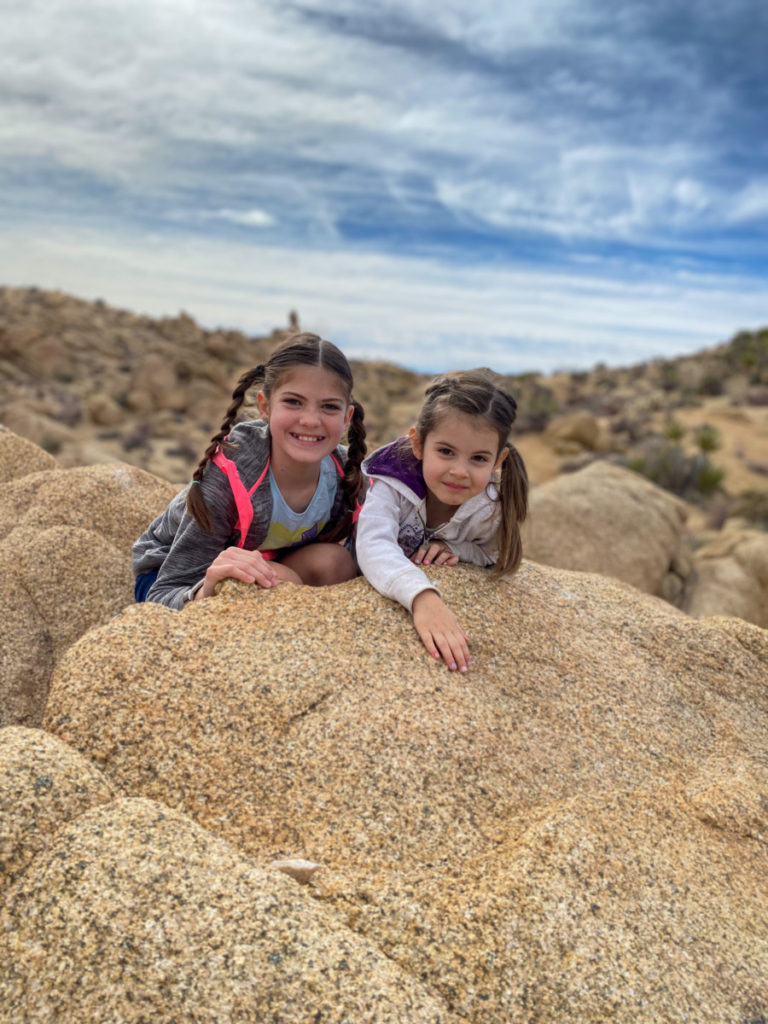 2 girls smile on a boulder with the view of the Mojave Desert behind them
