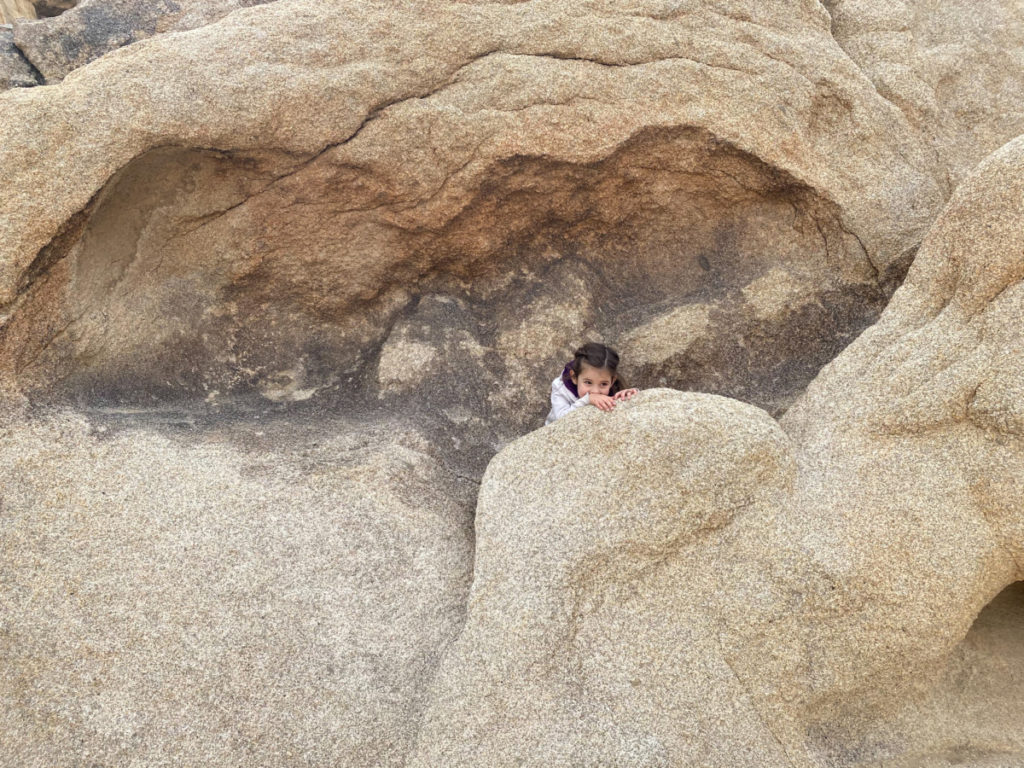 girl peeks out of a rock cavity at Joshua Tree